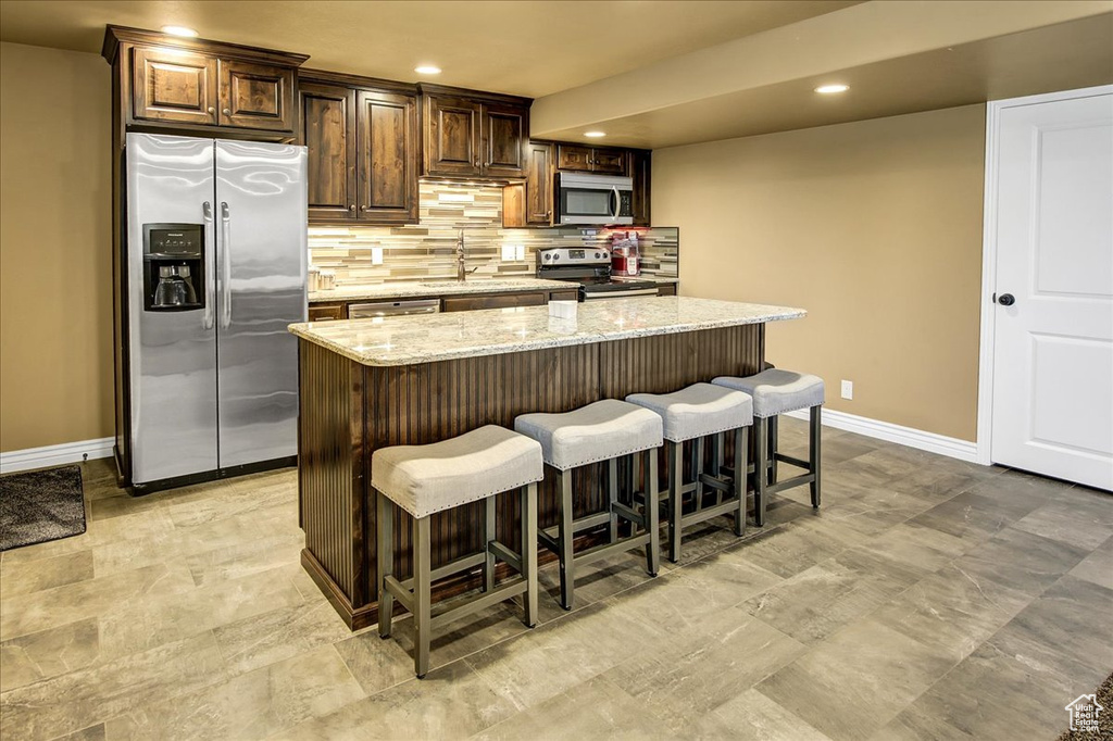 Kitchen featuring appliances with stainless steel finishes, baseboards, a breakfast bar, backsplash, and a center island