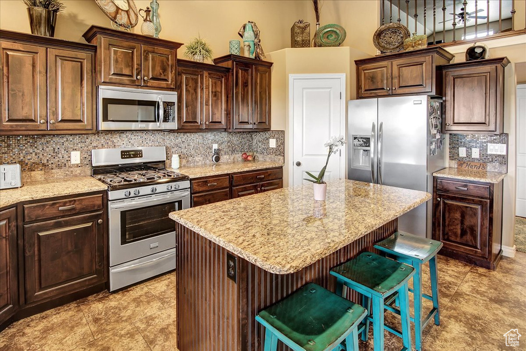 Kitchen featuring stainless steel appliances, a kitchen bar, backsplash, light stone countertops, and a towering ceiling