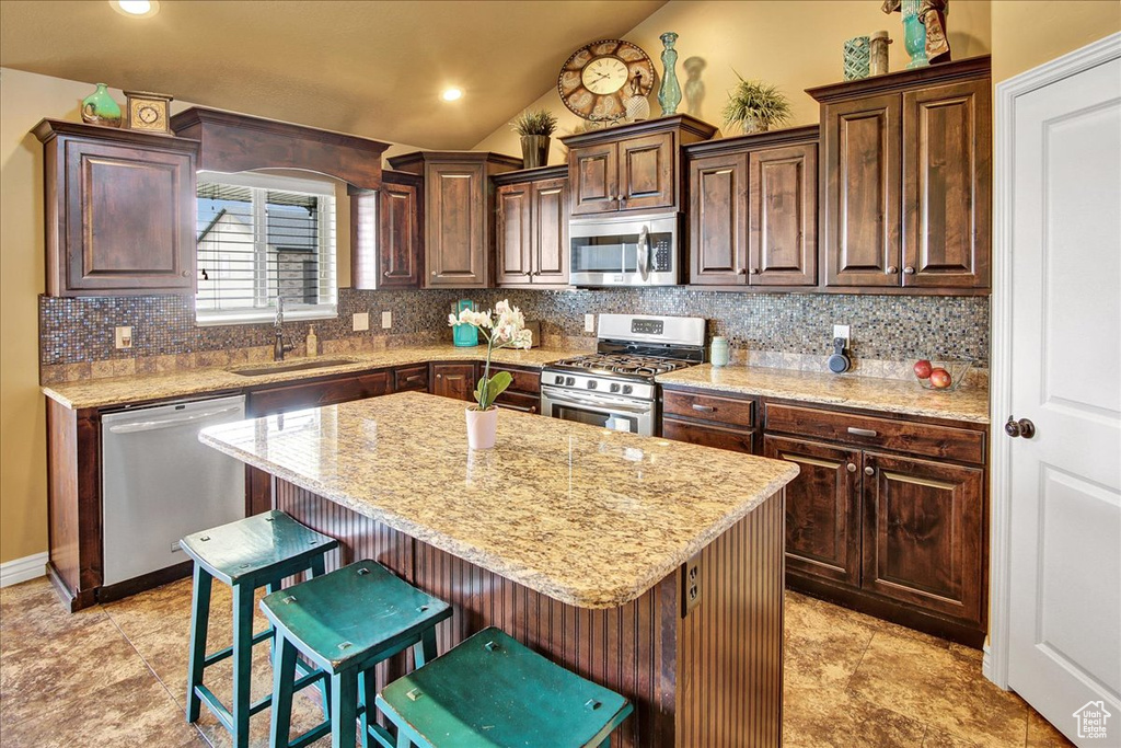 Kitchen with appliances with stainless steel finishes, a sink, decorative backsplash, lofted ceiling, and a kitchen breakfast bar