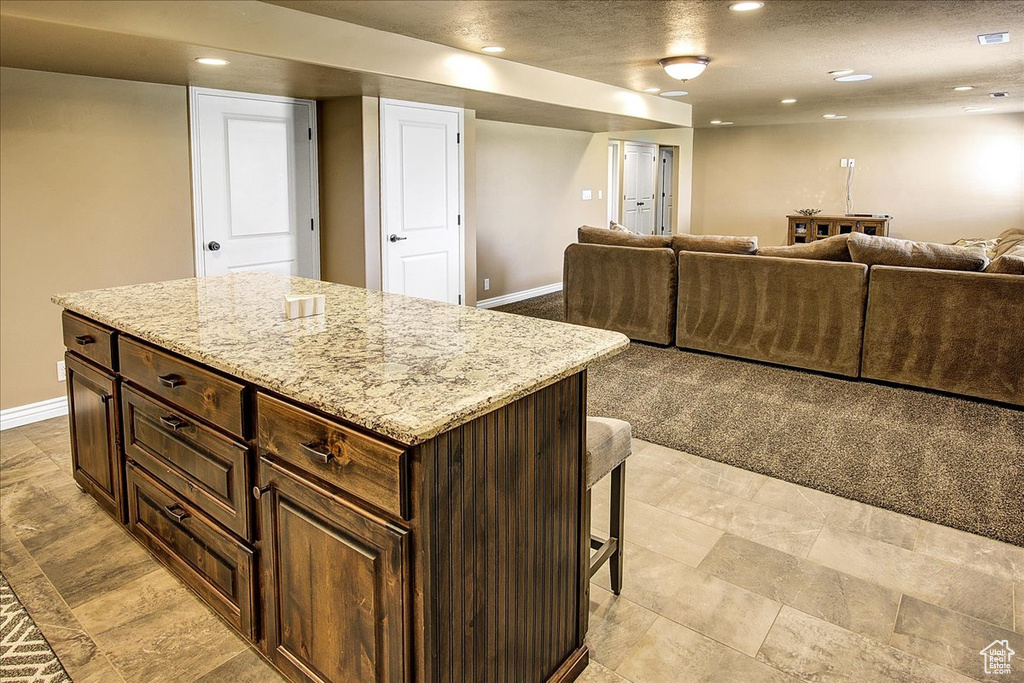 Kitchen with open floor plan, baseboards, a kitchen breakfast bar, recessed lighting, and light stone counters