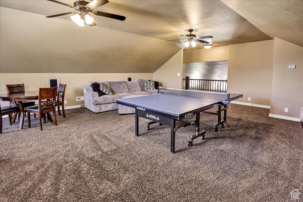 Rec room with a ceiling fan, vaulted ceiling, carpet floors, baseboards, and a textured ceiling