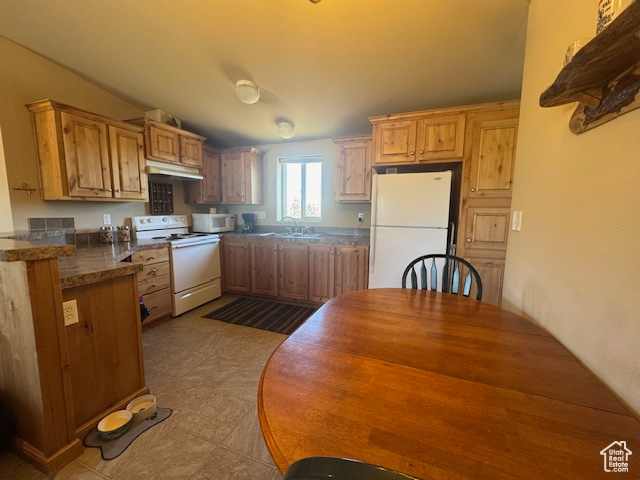Kitchen with white appliances, under cabinet range hood, dark countertops, and light tile patterned floors