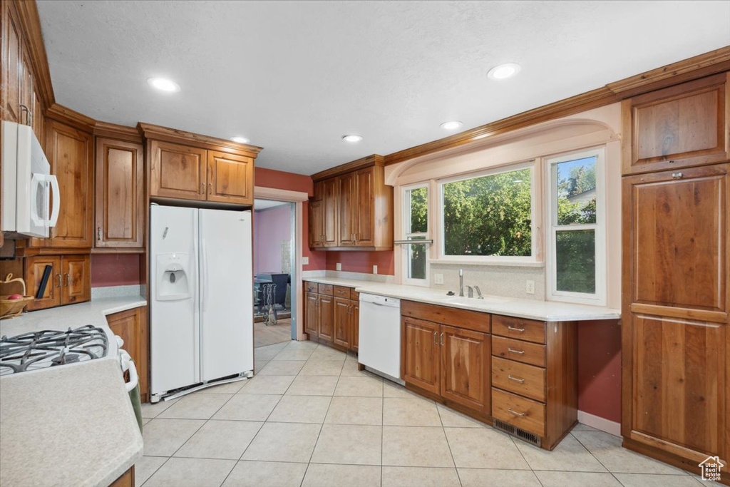 Kitchen with white appliances, light countertops, brown cabinetry, recessed lighting, and light tile patterned floors