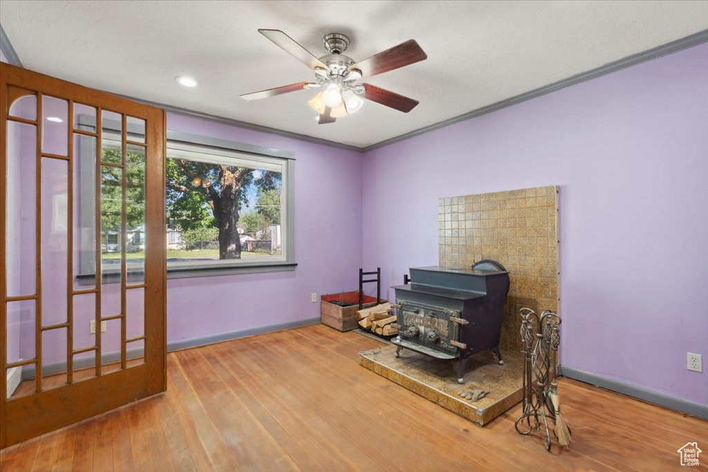 Interior space with a wood stove, a ceiling fan, wood finished floors, ornamental molding, and recessed lighting