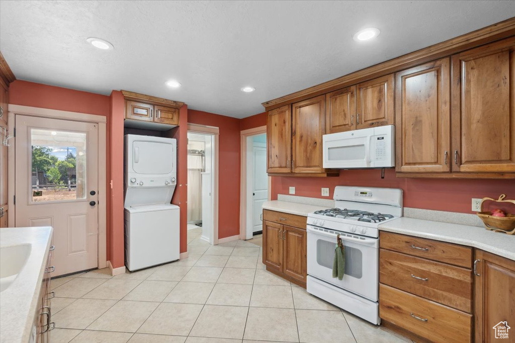 Kitchen featuring white appliances, stacked washer and clothes dryer, brown cabinets, light countertops, and recessed lighting