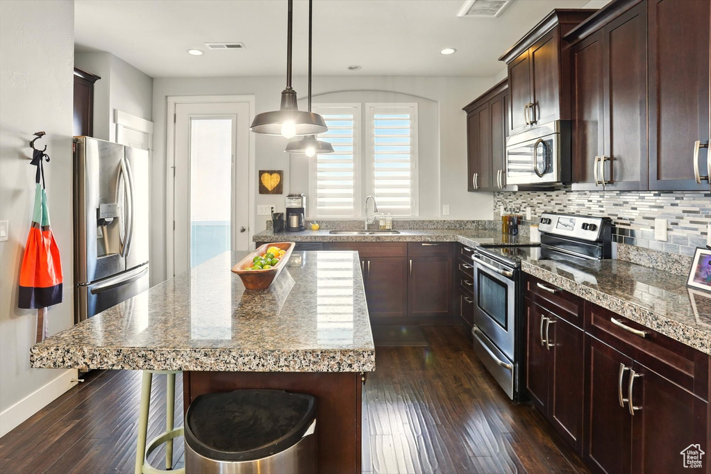 Kitchen featuring stainless steel appliances, a sink, a kitchen breakfast bar, dark wood-style flooring, and tasteful backsplash