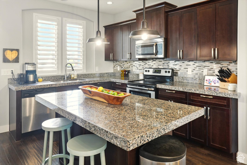 Kitchen featuring stainless steel appliances, a sink, a breakfast bar area, dark wood-style flooring, and dark brown cabinets