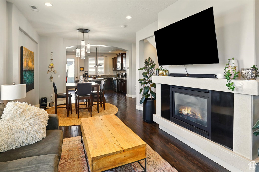 Living area featuring dark wood-style floors, recessed lighting, a glass covered fireplace, arched walkways, and baseboards