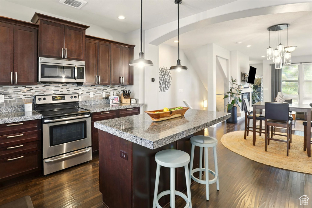 Kitchen featuring stainless steel appliances, dark wood-style floors, backsplash, a center island, and a breakfast bar