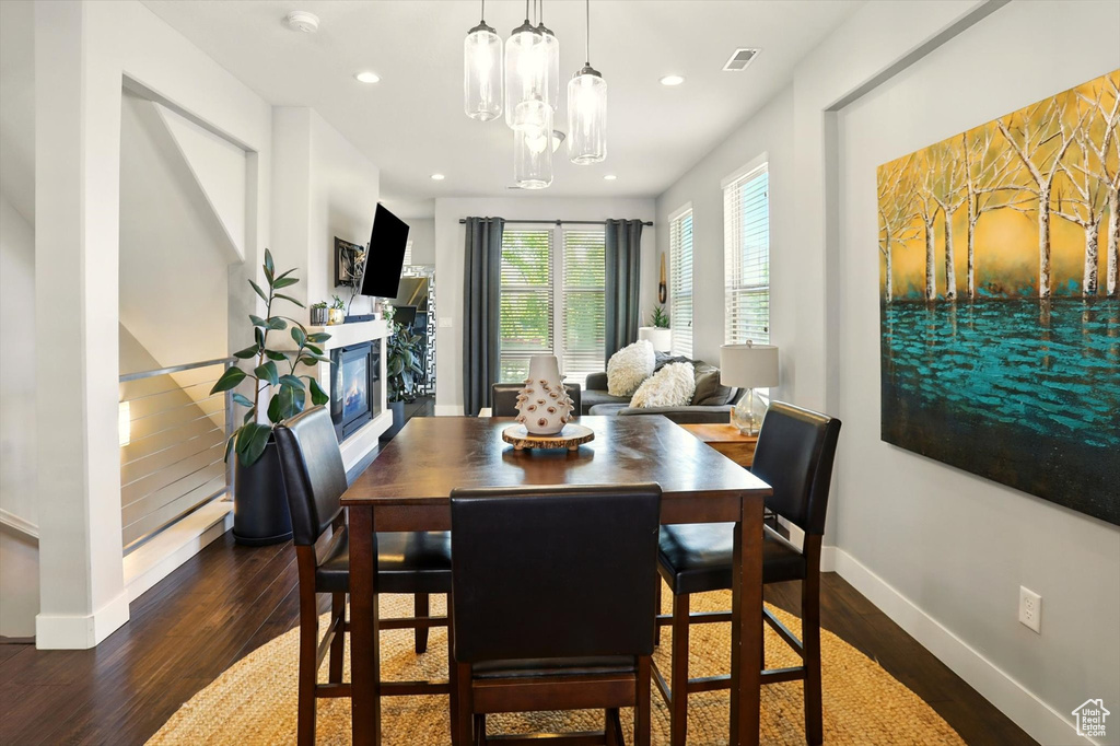 Dining space featuring dark wood-style flooring, baseboards, recessed lighting, a glass covered fireplace, and a chandelier