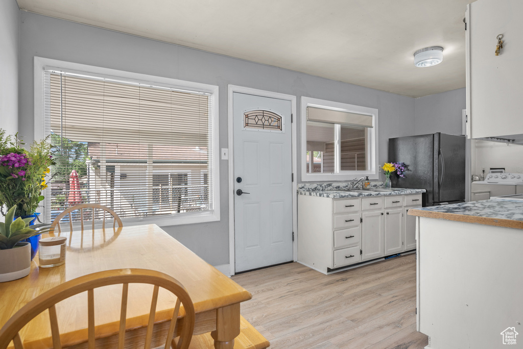 Kitchen with independent washer and dryer, freestanding refrigerator, white cabinetry, light wood finished floors, and light countertops