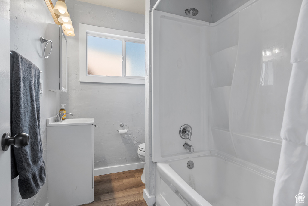Bathroom with baseboards, wood finished floors, vanity, shower / bath combo, and toilet