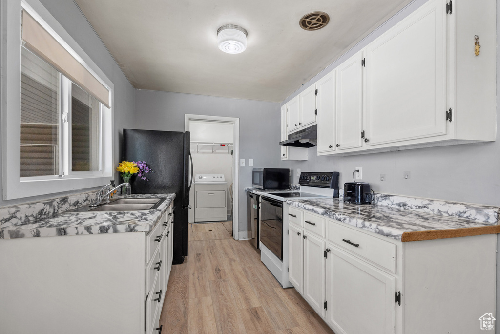 Kitchen with electric range oven, under cabinet range hood, washer / clothes dryer, a sink, and white cabinetry