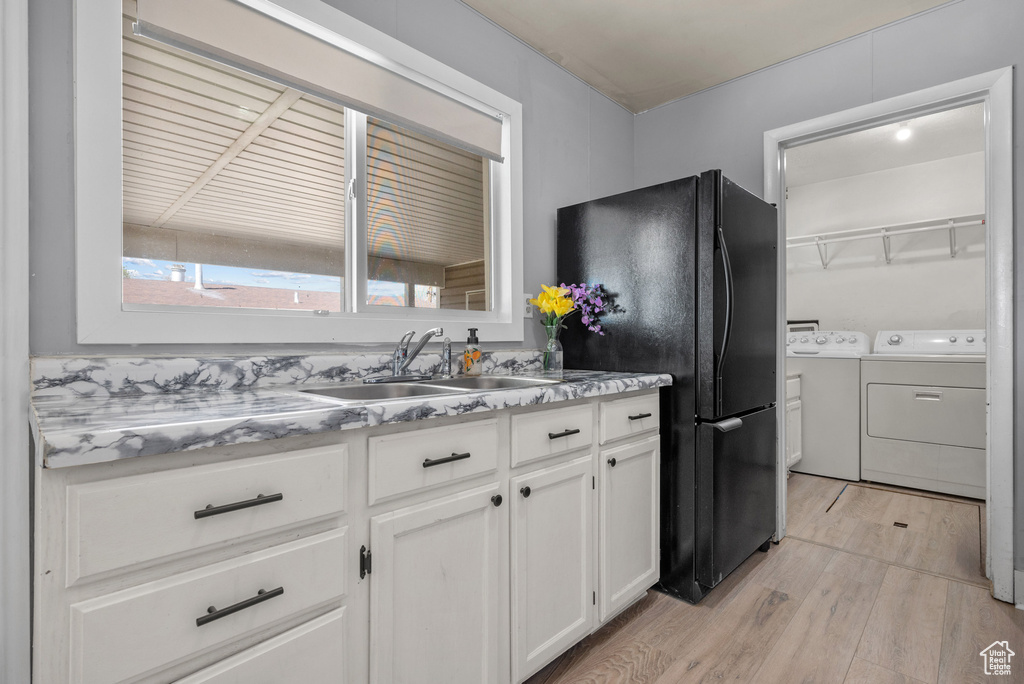 Kitchen with washer and clothes dryer, a sink, light wood-type flooring, white cabinets, and freestanding refrigerator