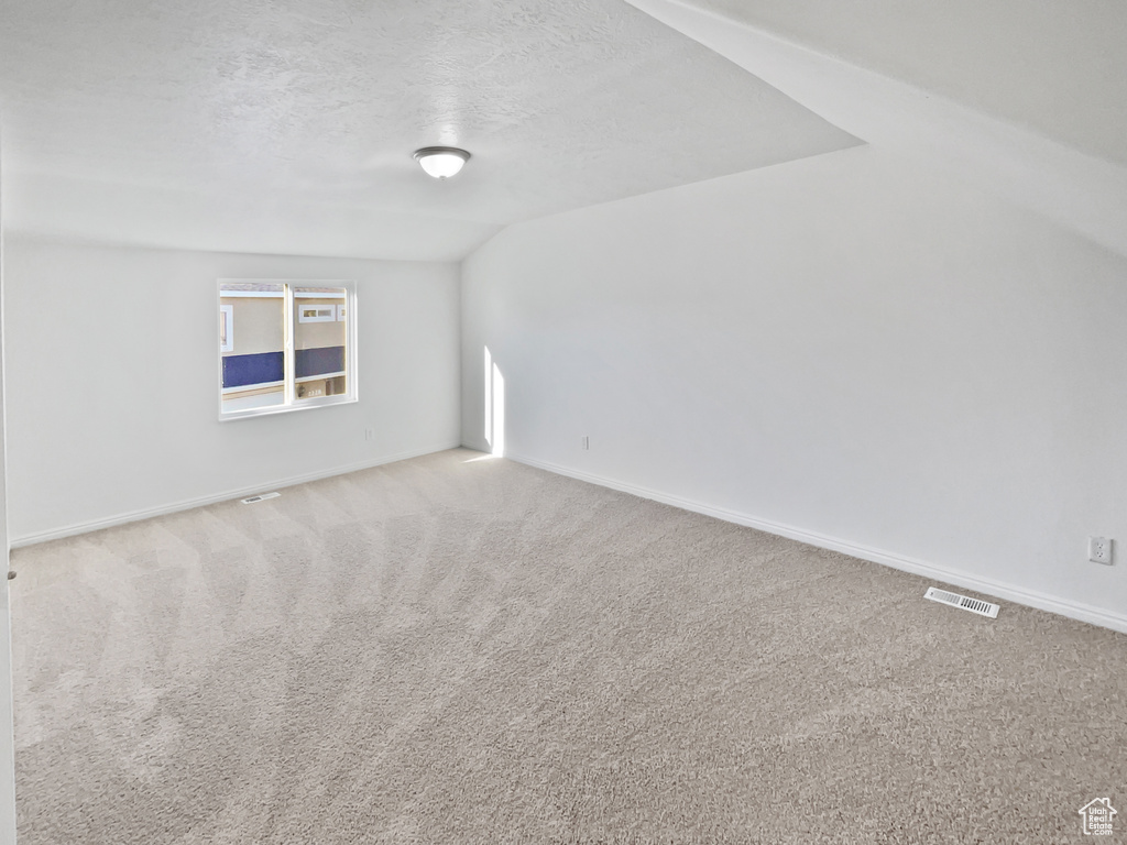 Carpeted empty room with a textured ceiling and vaulted ceiling