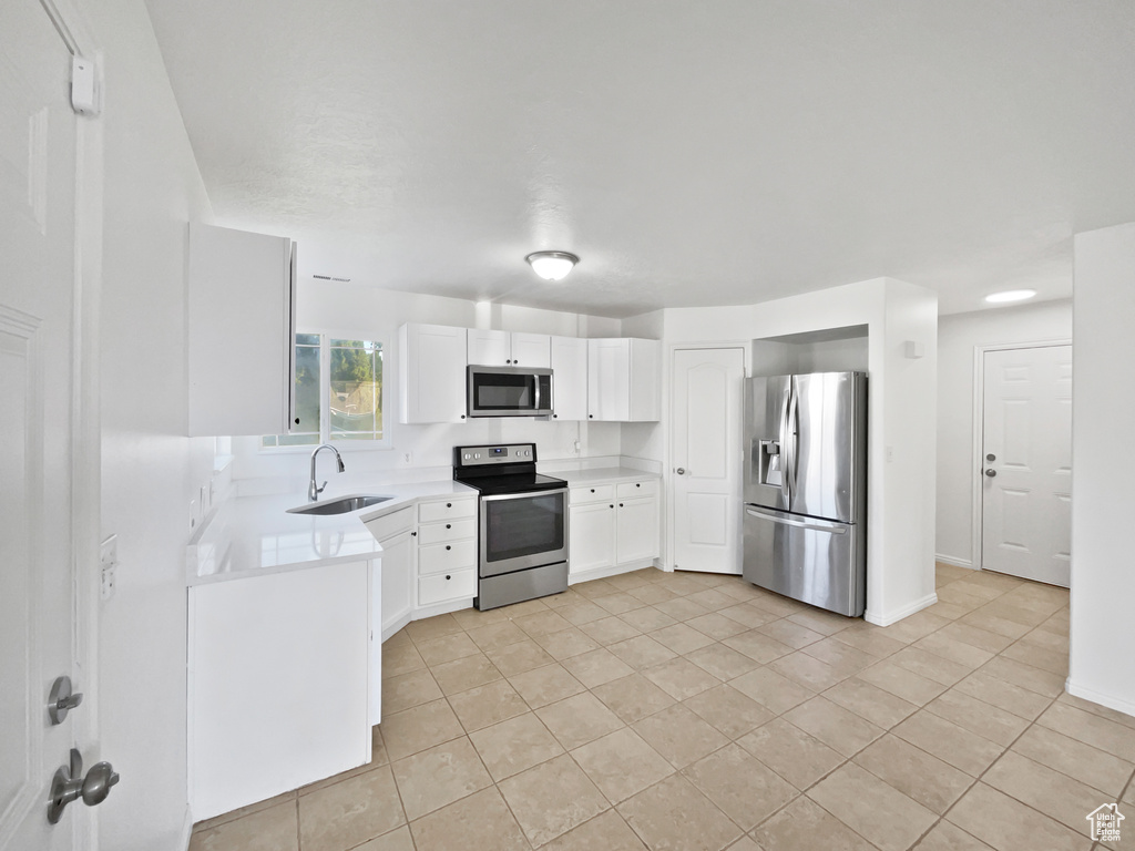 Kitchen with stainless steel appliances, light tile patterned floors, light countertops, and white cabinetry