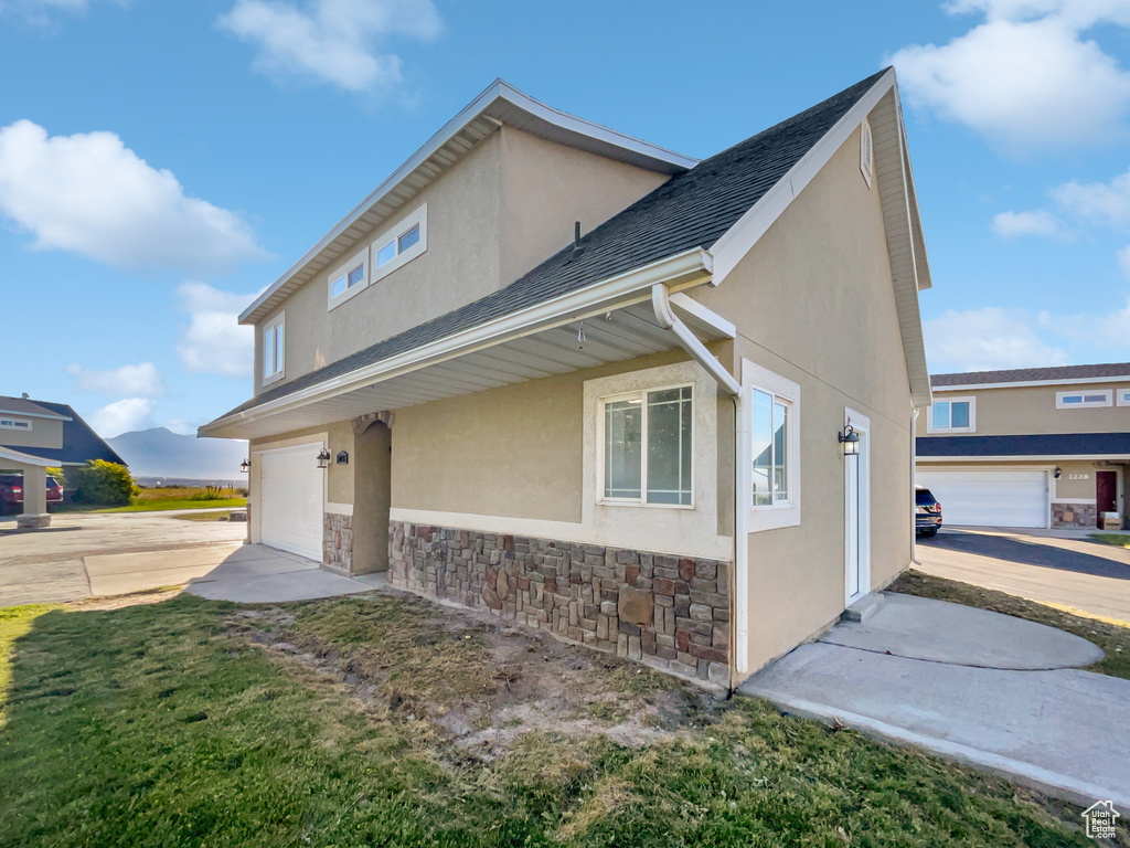 View of side of property with stone siding, stucco siding, an attached garage, and driveway
