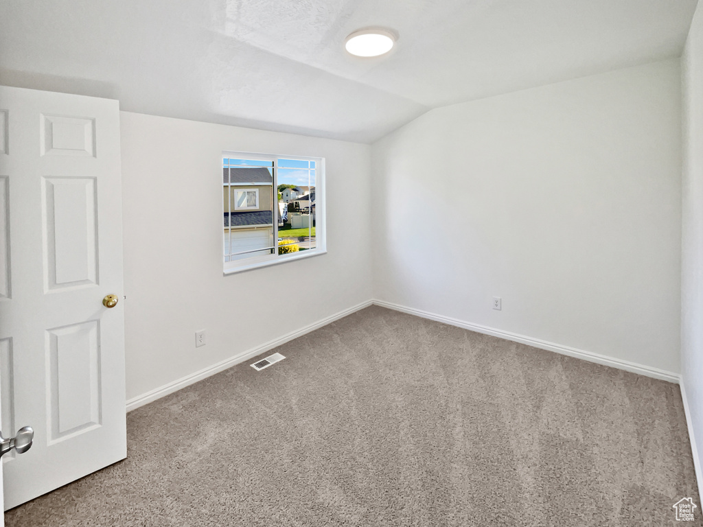 Carpeted empty room featuring vaulted ceiling and baseboards