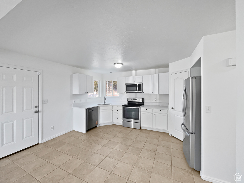 Kitchen with stainless steel appliances, light tile patterned floors, white cabinets, and light countertops
