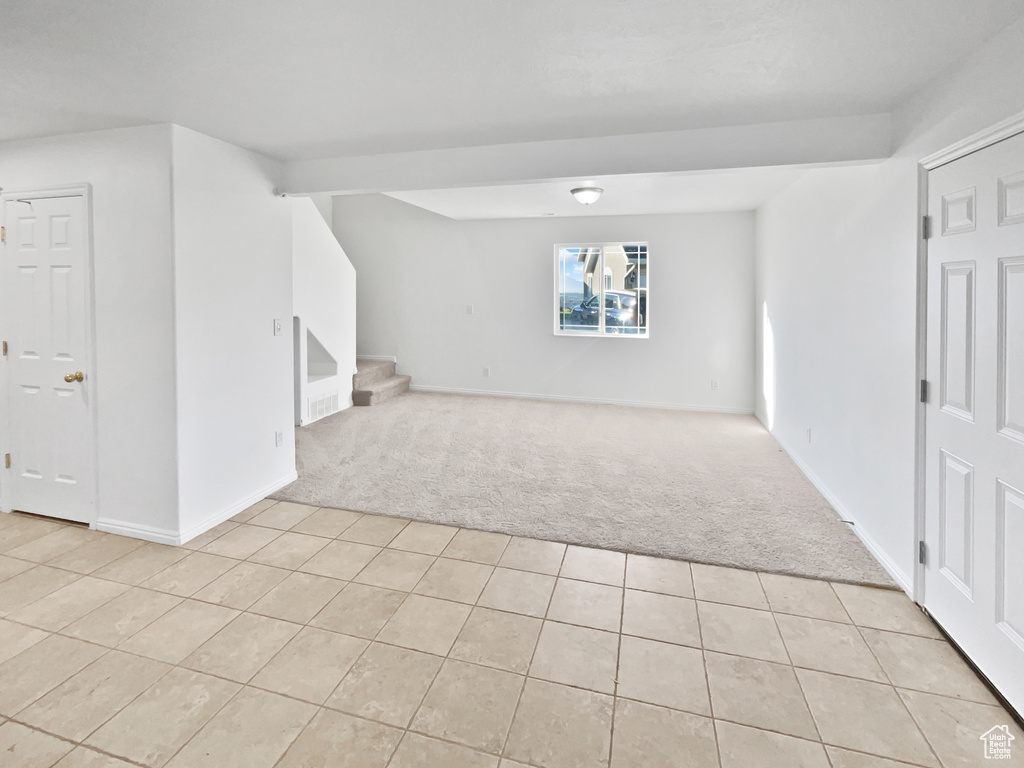 Unfurnished room featuring light colored carpet, light tile patterned floors, and stairs
