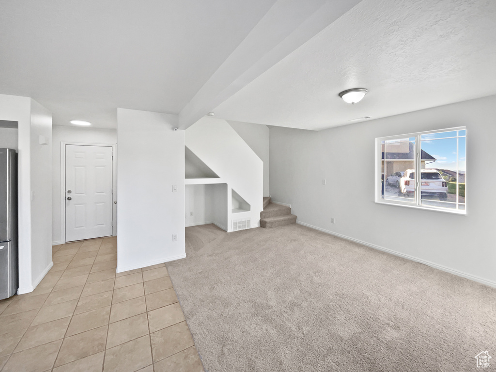 Basement with freestanding refrigerator, stairway, light tile patterned floors, and light carpet