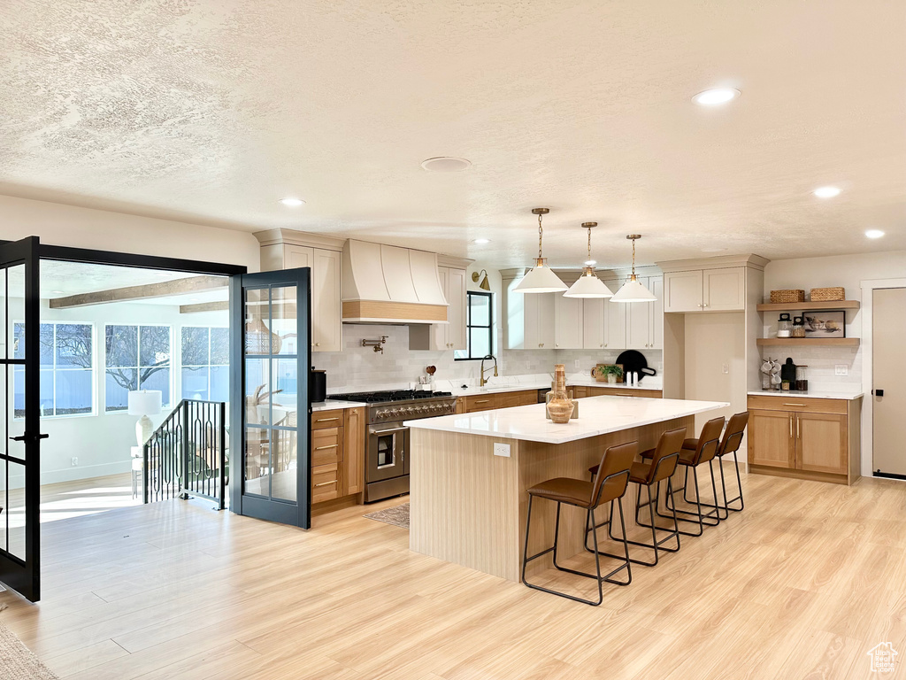 Kitchen with double oven range, custom range hood, light wood-type flooring, light countertops, and recessed lighting