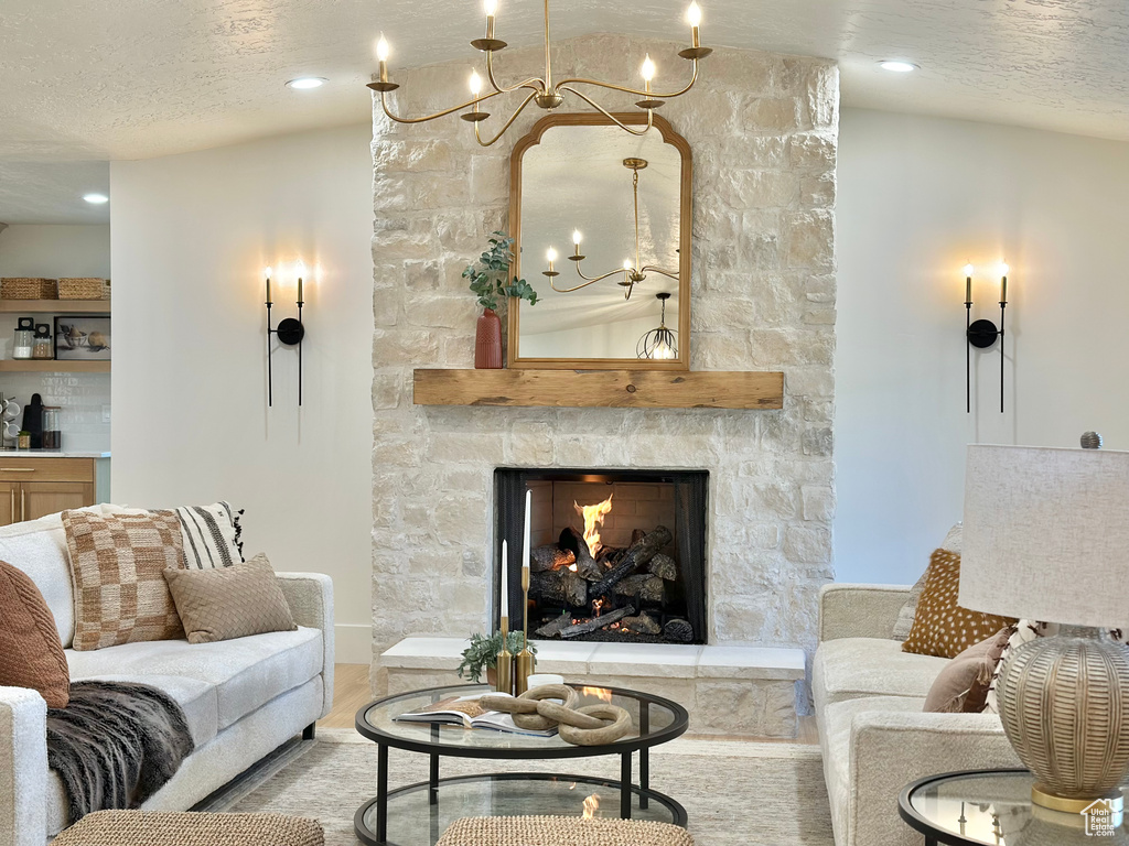 Living room with a chandelier, a stone fireplace, a textured ceiling, and wood finished floors