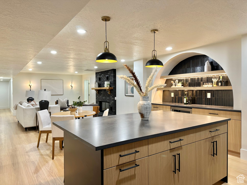 Kitchen with a textured ceiling, a center island, light wood-style flooring, recessed lighting, and dark countertops