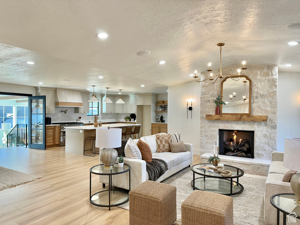 Living room featuring a textured ceiling, light wood finished floors, a chandelier, recessed lighting, and a fireplace
