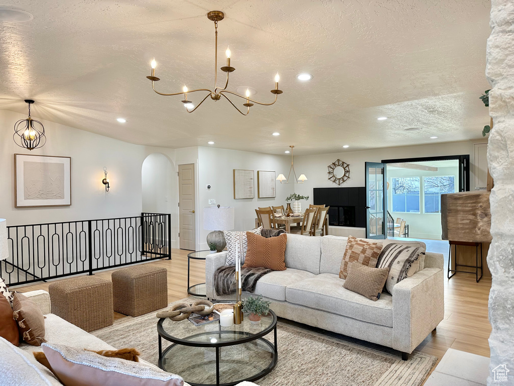 Living room featuring arched walkways, a chandelier, a textured ceiling, light wood-type flooring, and recessed lighting