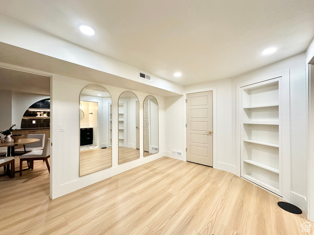 Basement with light wood finished floors, built in shelves, recessed lighting, and arched walkways
