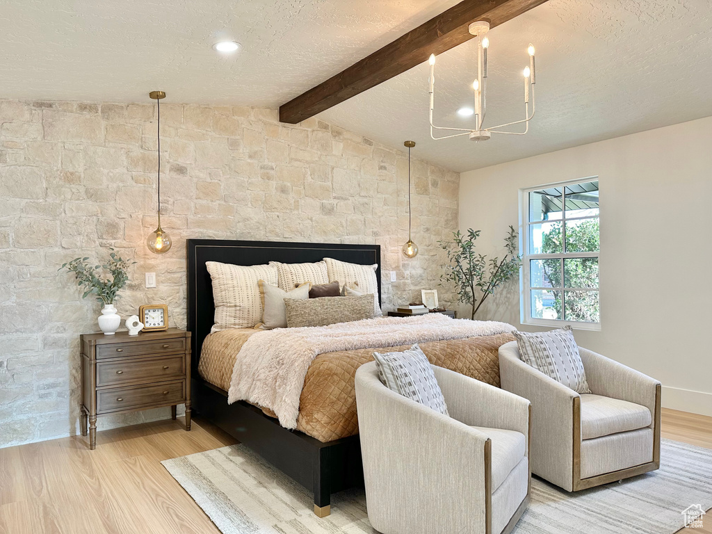 Bedroom with light wood-type flooring, a chandelier, a multi sided fireplace, and a textured ceiling