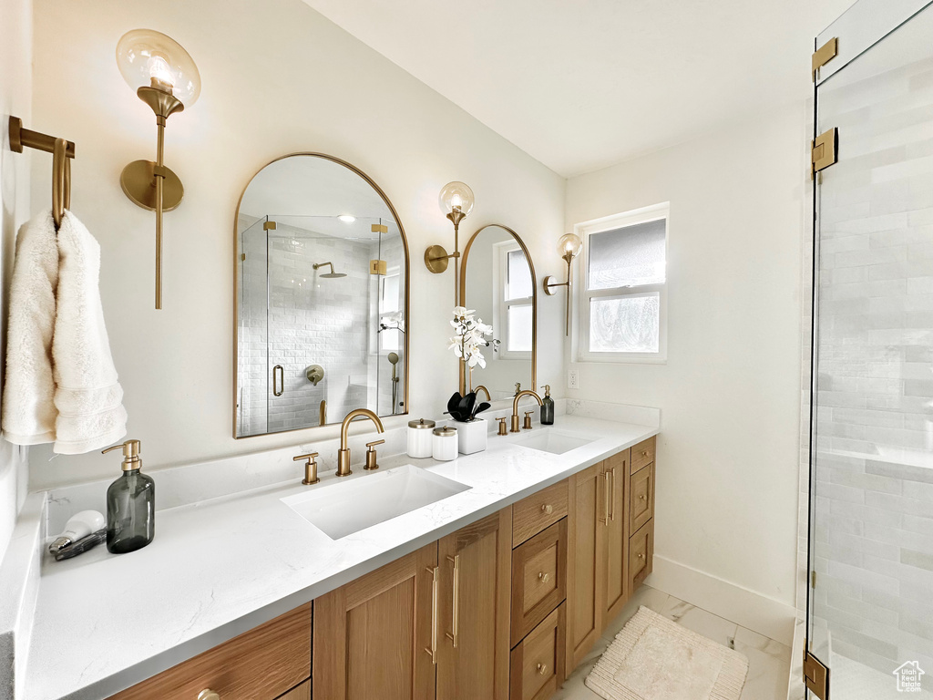 Full bath featuring double vanity, a stall shower, and marble look tiles