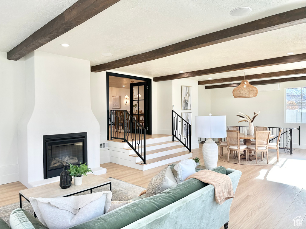 Living room with beamed ceiling, light wood-style flooring, a glass covered fireplace, and recessed lighting