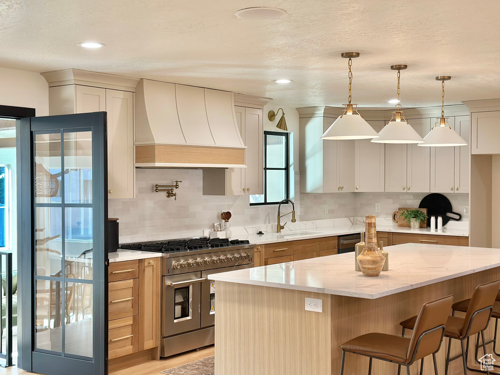 Kitchen with premium range hood, double oven range, decorative backsplash, light stone counters, and dishwashing machine