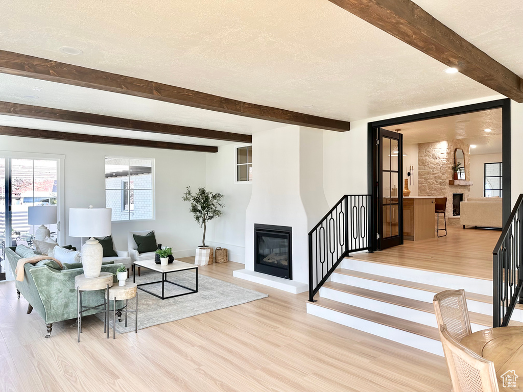 Living room featuring a fireplace, light wood-type flooring, beamed ceiling, stairs, and a textured ceiling