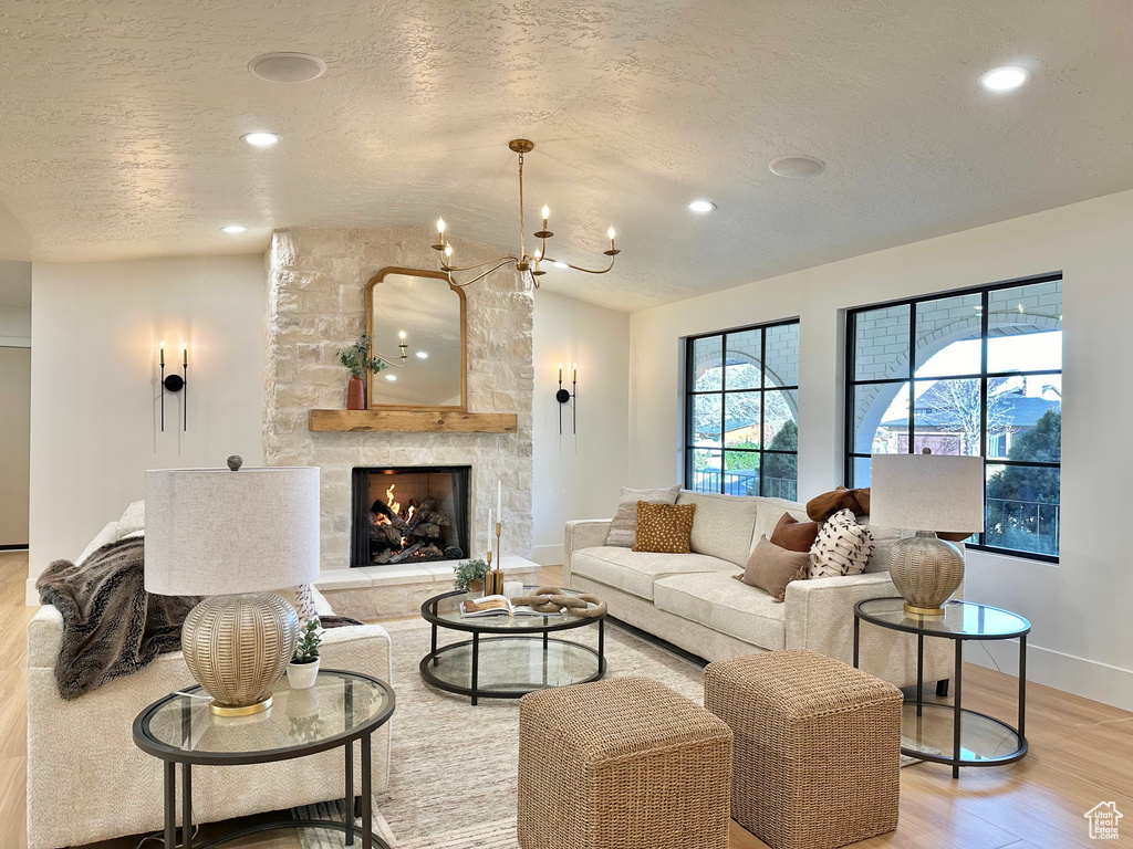 Living area with light wood finished floors, a textured ceiling, recessed lighting, a stone fireplace, and a chandelier