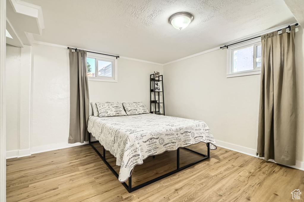 Bedroom featuring light wood finished floors, baseboards, a textured ceiling, and ornamental molding