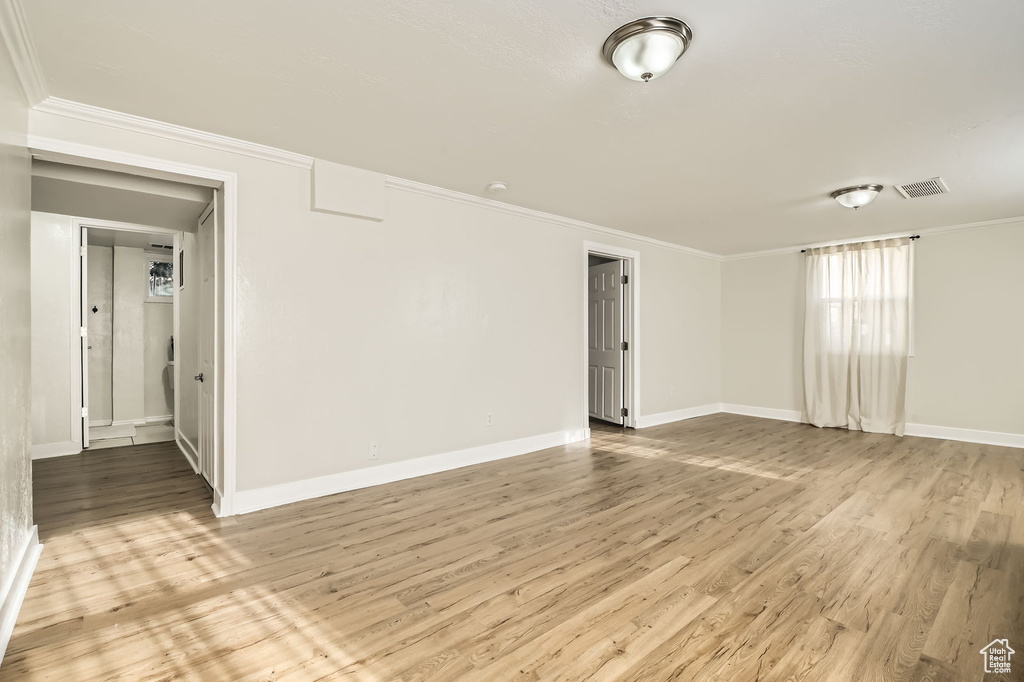 Empty room featuring light wood-style floors, baseboards, and crown molding