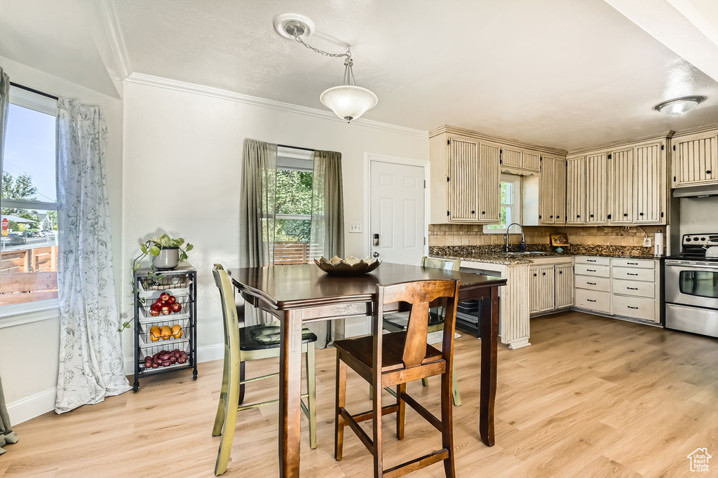 Kitchen with stainless steel electric stove, cream cabinetry, dark countertops, light wood-style floors, and crown molding