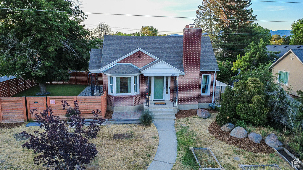 Bungalow-style home with a chimney, roof with shingles, and brick siding