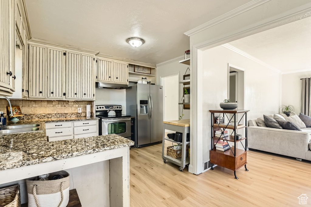 Kitchen with stainless steel appliances, a sink, under cabinet range hood, cream cabinets, and light wood-style floors