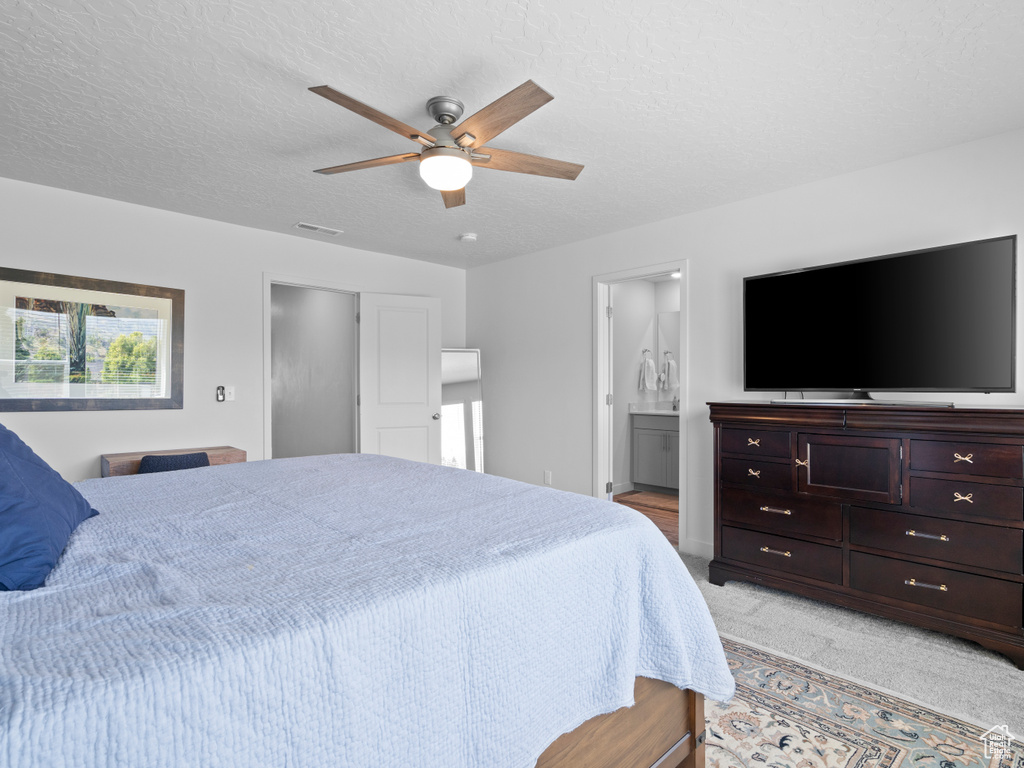 Bedroom featuring a textured ceiling, light carpet, connected bathroom, and a ceiling fan