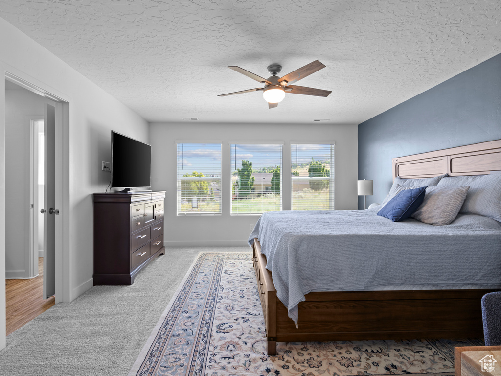 Bedroom with light carpet, ceiling fan, and a textured ceiling