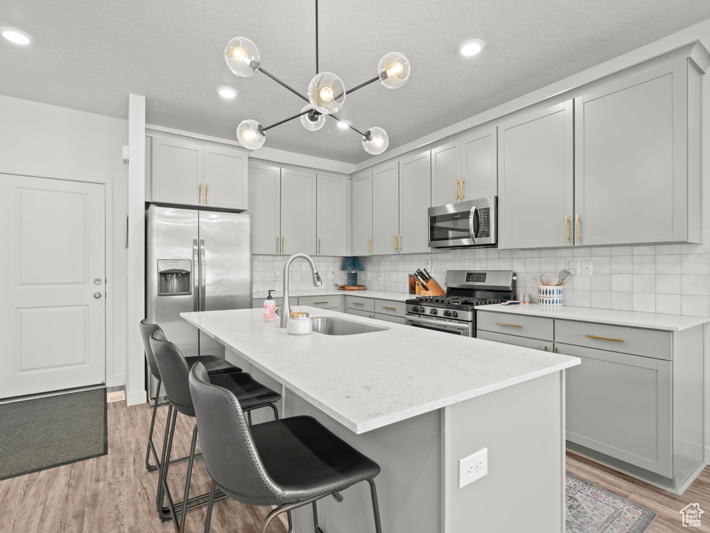 Kitchen featuring appliances with stainless steel finishes, a breakfast bar, tasteful backsplash, light wood-style flooring, and a kitchen island with sink