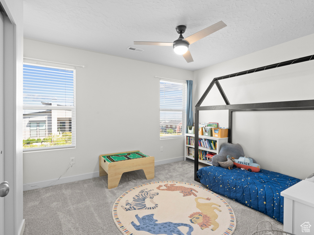 Carpeted bedroom with multiple windows, a textured ceiling, and ceiling fan