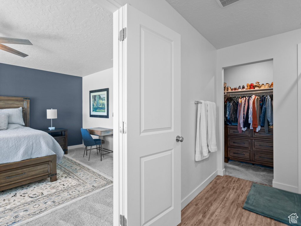 Bedroom featuring a walk in closet, a textured ceiling, a closet, wood finished floors, and a ceiling fan