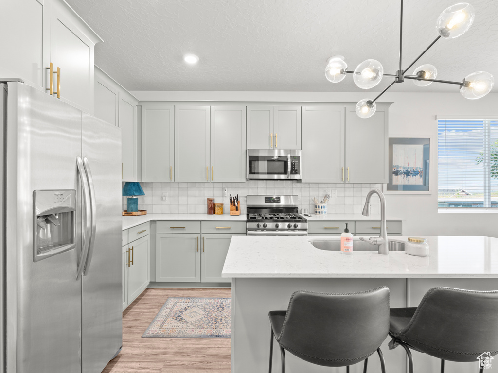 Kitchen with appliances with stainless steel finishes, light wood-style flooring, tasteful backsplash, decorative light fixtures, and a breakfast bar area