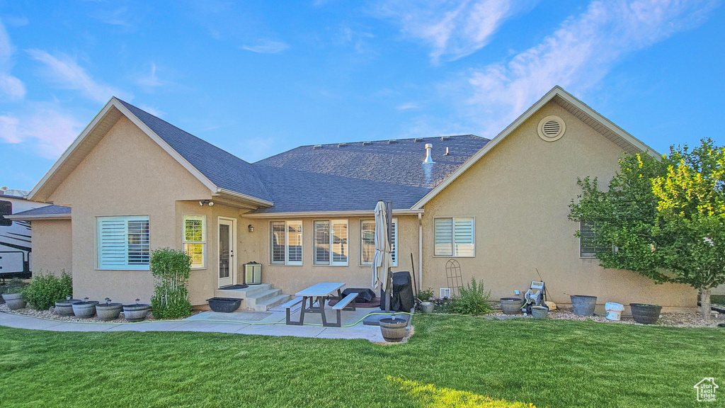 Rear view of property featuring stucco siding, a yard, a patio, and a shingled roof