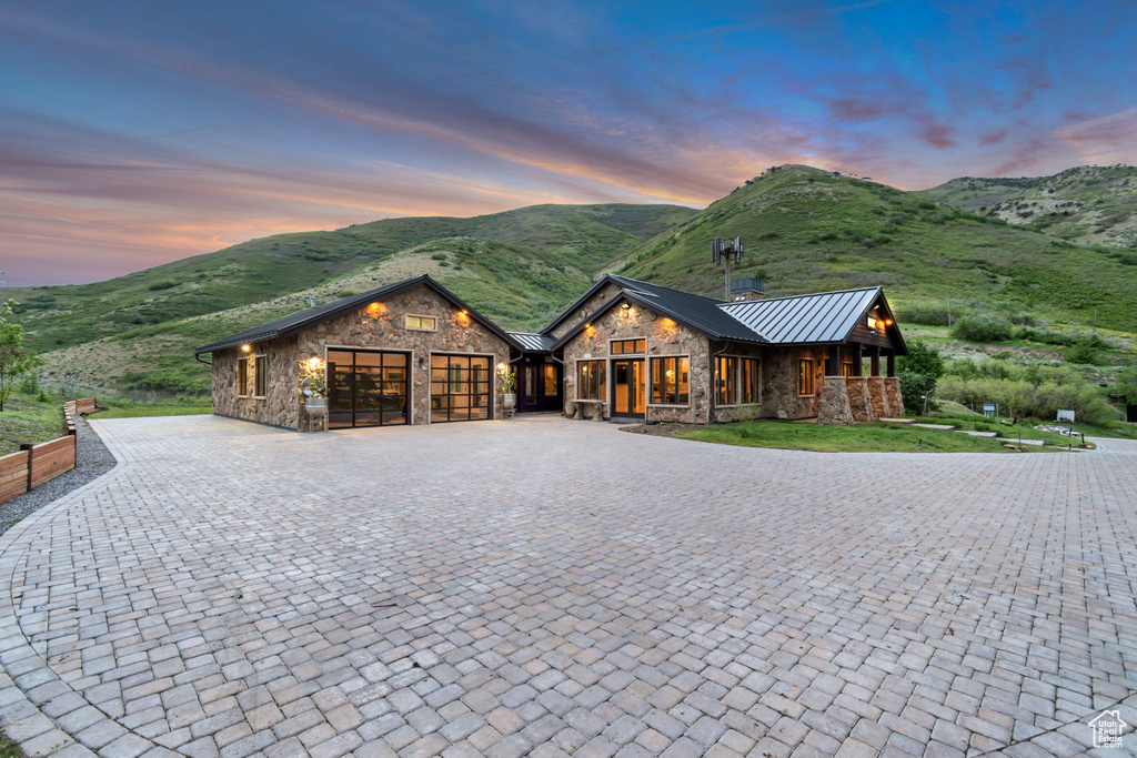 Rustic home featuring stone siding, a standing seam roof, an attached garage, and curved driveway
